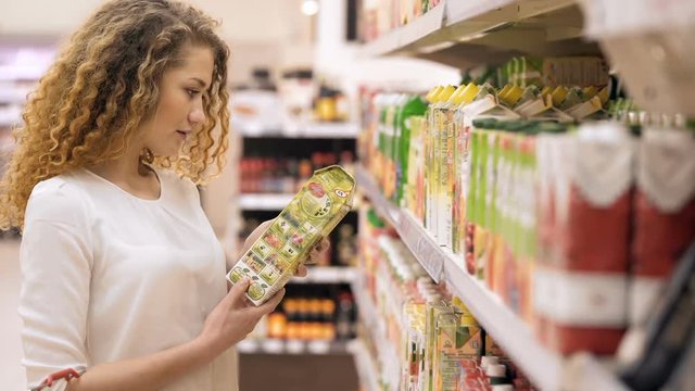 Woman chooses juice in the supermarket. Woman Choosing Products in Shopping Mall. Girl stands near the store shelf and selects the products