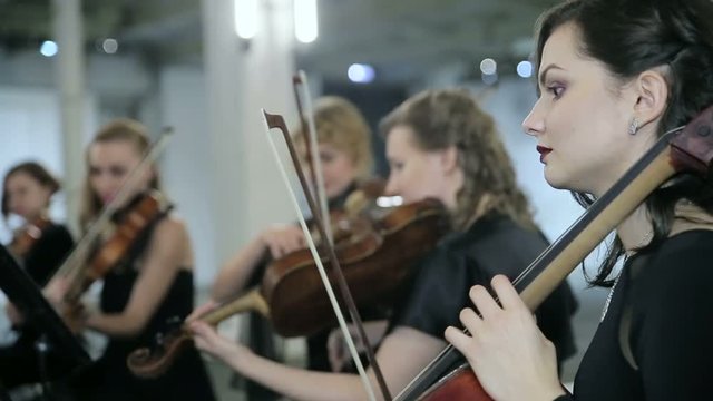 Girls play on violoncello in orchestra
