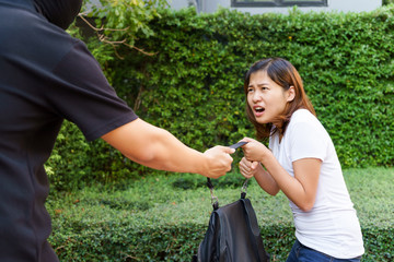 Thief stealing and jerking handbag from young woman at public park.