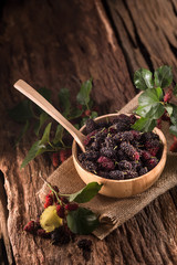 Mulberry berries in a wooden cup on a wooden background