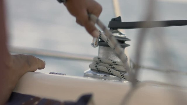 Hands pulling ropes, winding sheets around winches on yacht