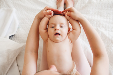 Closeup portrait of  cute adorable white Caucasian newborn baby lying on mother lap doing physical exercises together, funny face expression, early development concept