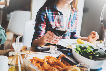 People celebrating with glasses of red wine and homemade food, cozy atmosphere, young group of hipsters have fun at modern cafe with healthy food, filtered image, enjoyment and holidays concept