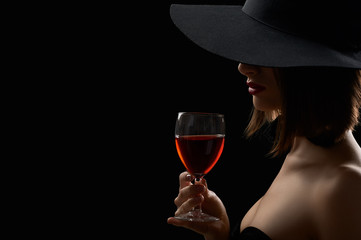 Elegant mysterious woman in a hat holding a glass of red wine on