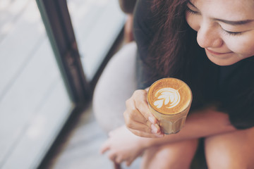 Closeup image of Asian woman holding coffee cup and smelling hot coffee with feeling good in cafe