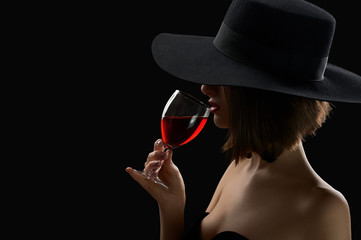 Elegant mysterious woman in a hat holding a glass of red wine on