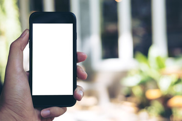 Mockup image of hand holding black mobile phone with blank white screen in loft cafe and green nature
