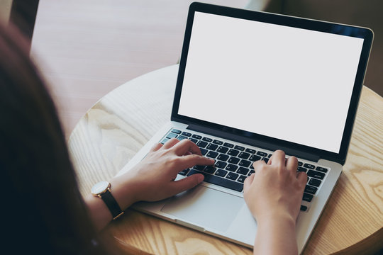 Mockup image of hands using laptop with blank white screen on vintage wooden table in cafe