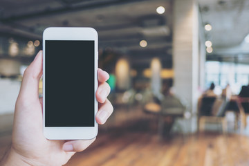 Mockup image of hand holding white mobile phone with blank black screen in vintage wooden cafe
