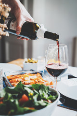 Vertical image of men’s hand pouring red wine, enjoyment and celebrating concept, festive table on the background