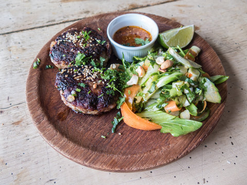 Spicy lamb meat patties, burgers with a cashew nut and green salad served with a salsa dip in a pot and a lime slice on a wooden rustic dish on a wooden table.