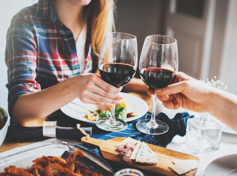 Young romantic couple celebrating with glasses of red wine, Happy couple making cheers at restaurant, cozy atmosphere, holidays and enjoyment concept