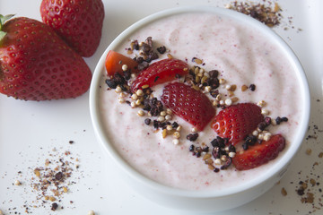 Greek strawberry yoghurt served in a bowl with strawberries and a superfruit topping of dried blueberries, hibiscus, chia seeds and airy quinoa pops