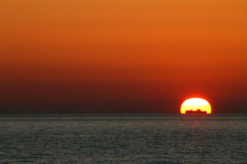 Fototapeta na wymiar Sunset on the mediterranean sea with a ship passing in front of the sun