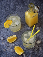 Two glasses of cold homemade lemonade with lemon slices, ice cubes and straws on dark background. Copy space