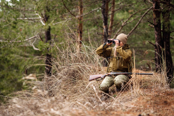 Female hunter in camouflage clothes ready to hunt, holding gun and walking in forest.