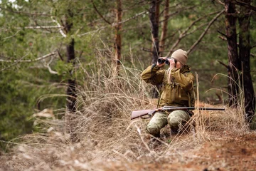 Photo sur Plexiglas Chasser Chasseuse en tenue de camouflage prête à chasser, tenant une arme à feu et marchant dans la forêt.