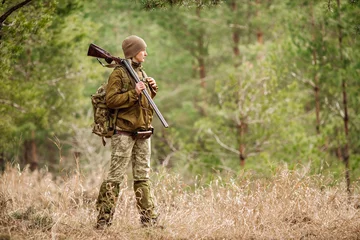 Store enrouleur tamisant Chasser Female hunter in camouflage clothes ready to hunt, holding gun and walking in forest.