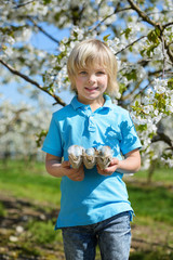 Happy little boy  with easter eggs in blossoming cherry garden