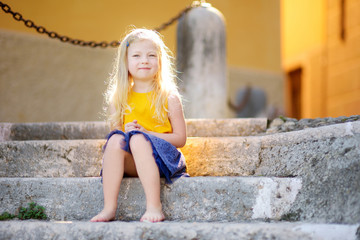 Adorable little girl sitting on the stairs on warm and sunny summer day © MNStudio