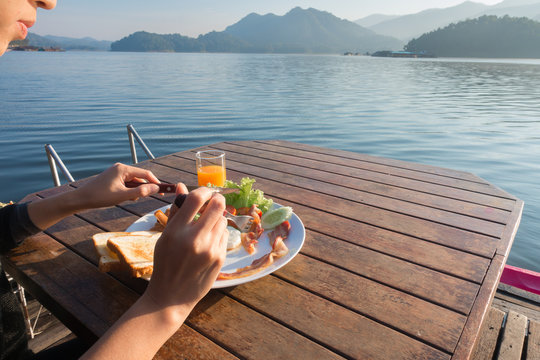 Close up cute girl eating breakfast food with orange juice on wooden table at beautiful lake ,Mae Ngat dam, Chaing Mai, Thailand