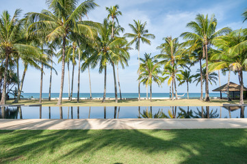 Fototapeta premium Swimming pool with coconut tree and sea background, reflection of coconut trees and white cloud and blue sky on the swimming pool at the beach