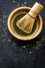 Matcha green tea in a bowl and bamboo whisk on black slate
