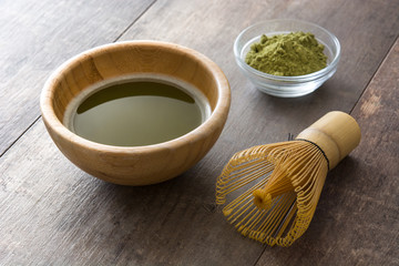 Matcha green tea in a bowl and bamboo whisk on wooden table
