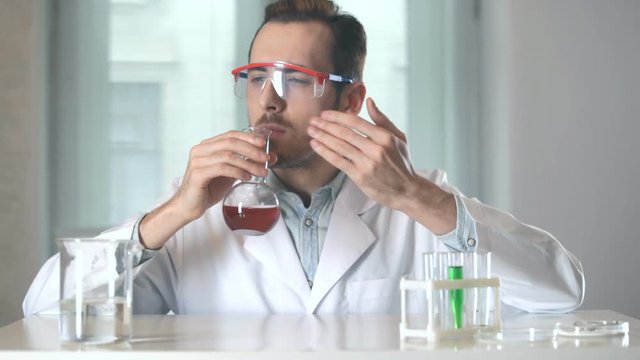 perfumer inhales the scent from the flask. scientist stirs and sniffs the liquid inside the flask.