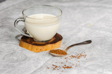 A cup of glass milk for cappuccino. Spoon with coffee.