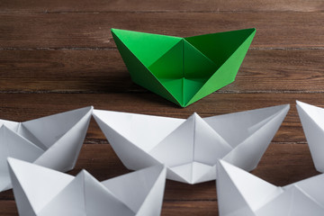 Business leadership concept with white and color paper boats on wooden table