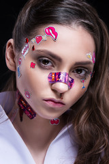 Beautiful fashion girl with luxury professional makeup and funny emoji stickers glued on the face.