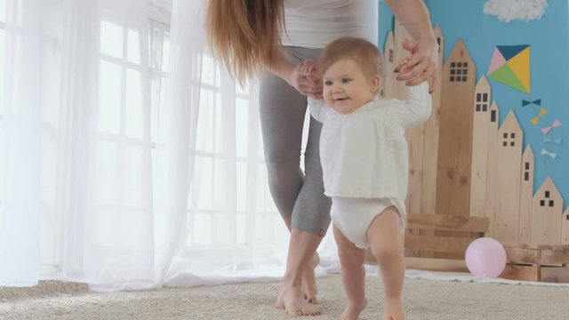 happy little baby learning to walk with mother help at home