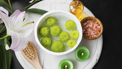 Relaxing spa setting with water bowl and green flowers,oil, salt, candles and lily flower, top view