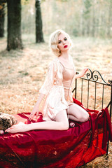 Beautiful and elegant blonde woman with red lips and hair waves wearing beige nightie posing on the...