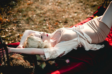 Beautiful and elegant blonde woman with red lips and hair waves wearing beige nightie posing on the...