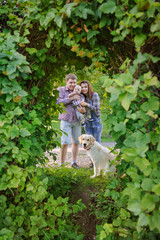 Fototapeta premium Family of three with a dog in the park, mother and father holding a child
