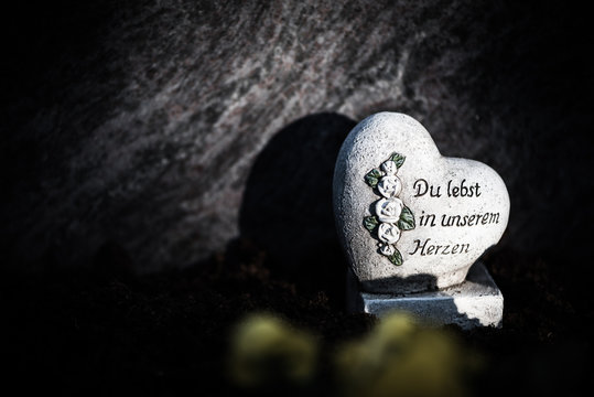 Herz aus Stein mit der Inschrift "Du lebst in unserem Herzen" auf einem Grab