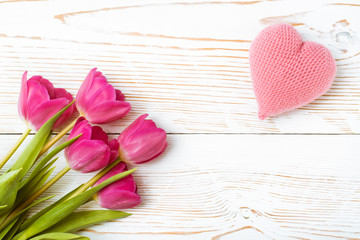 Букет свежих тюльпанов и розовое вязанное сердце на белом деревянном фоне