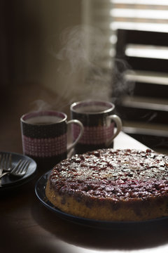 Cranberry upside-down cake on plate, hot drinks on table beside cake
