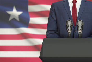 Businessman or politician making speech from behind a pulpit with national flag on background -...