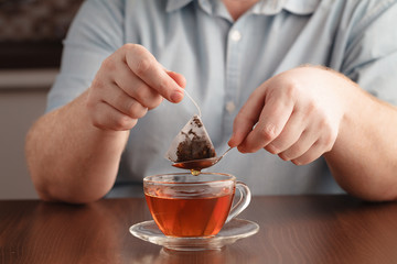man brewing tea bag with glass of tea on table