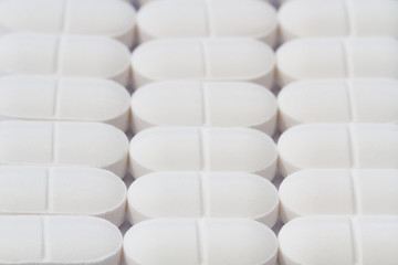 Rows of white drugs, pills, tablets and medicines on a white background representing pharmaceutical and drug production.