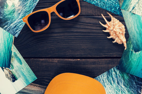 Sunglasses, shell, cap, and pictures with the image of the sea on a wooden surface