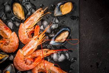 Prepared for cooking dinner seafood - shrimp and mussels on ice, on a cutting slate board, with lemon and seasonings. Top view, copy space