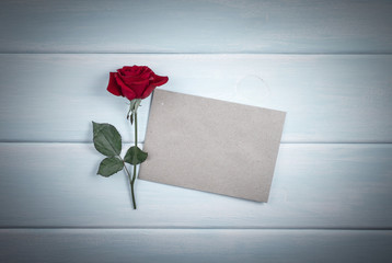 Red rose with paper card on wooden planks