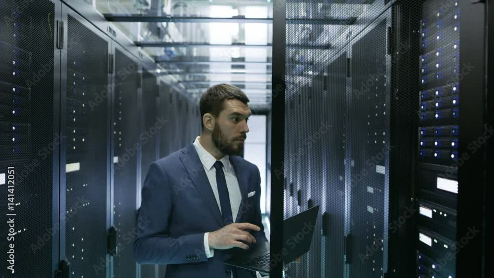 Poster it engineer in data center stands before server rack cabinet working on his laptop. runs diagnostics