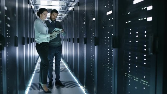 Male and Female Server Technicians Working in Data Center. Running Rack Server Diagnostics. Woman Uses Tablet Computer. Shot on RED EPIC-W 8K Helium Cinema Camera.