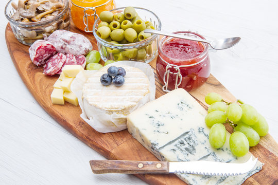 wooden cutting board with cheese, cold cuts and jams