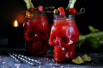 Bloody Mary cocktail in glasses-skull with celery sticks, pink salt, lime and canapes from canned vegetables.